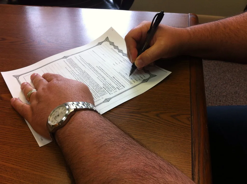 Mano firmando un contrato impreso sobre un escritorio de madera