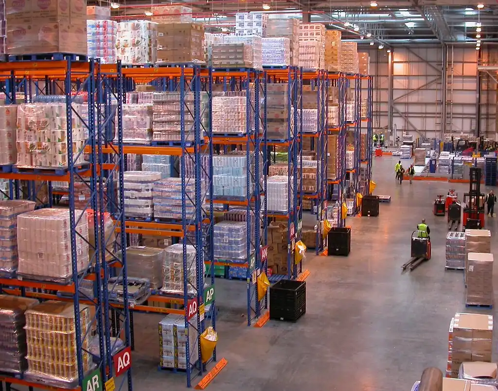 Centro de distribución con tarimas de inventario en racks y montacargas en el pasillo