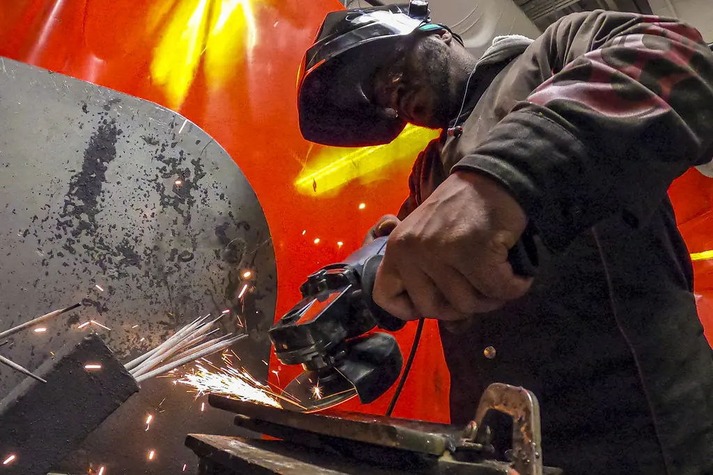 Trabajador con careta cortando metal con una esmeriladora que lanza chispas