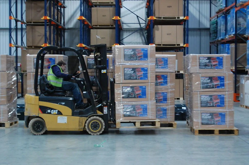Montacargas moviendo tarimas con cajas entre racks de un almacén